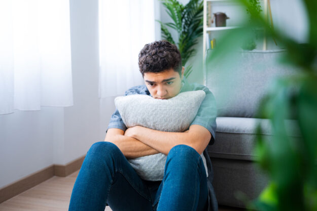 a person sits on the floor and hugs a pillow while dealing with untreated bipolar disorder