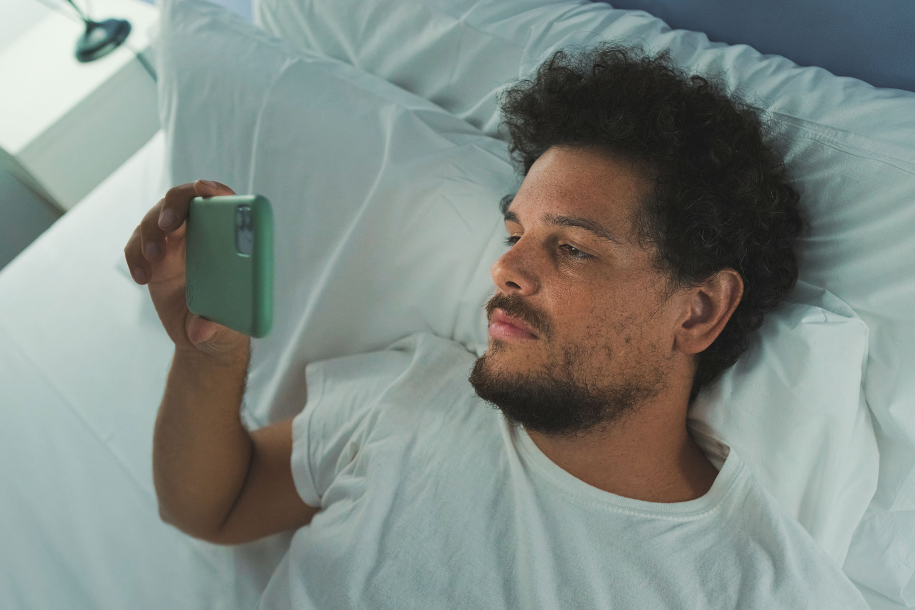 a person lays in bed looking at their phone wondering about screen time and mental health